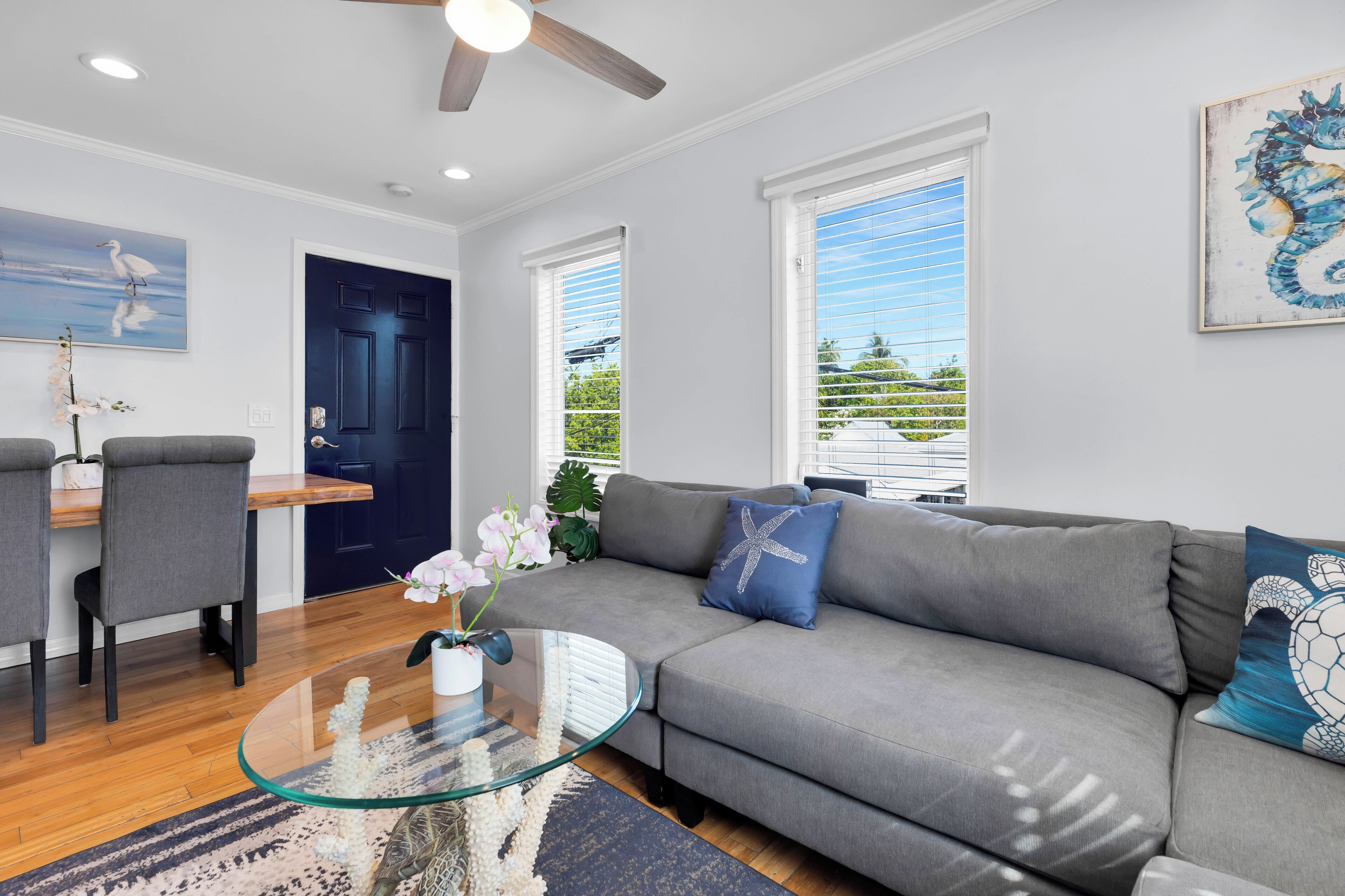 A modern living room with a grey sofa, a glass coffee table, and a ceiling fan.