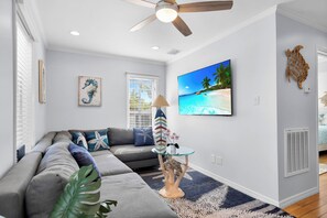 A modern living room with a sectional sofa, a glass coffee table, and a beach-themed painting. - Old Town Apartment with Parking, Walk to the Beach (Key West)