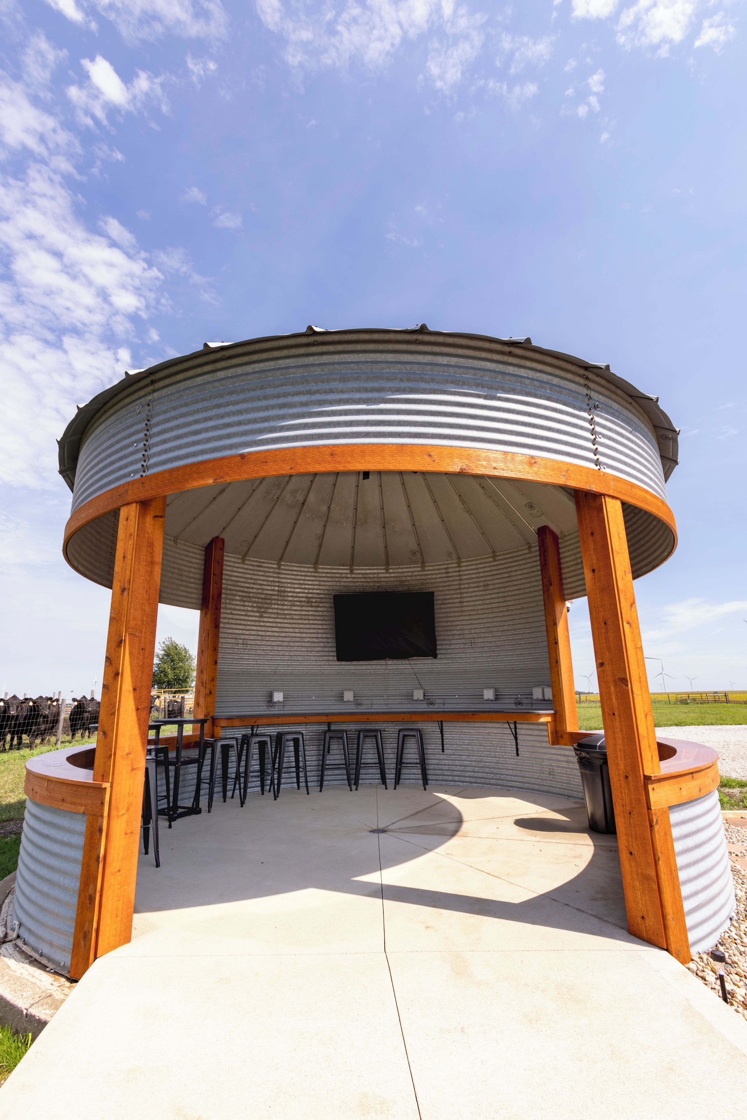 A circular outdoor structure with a flat roof, wooden posts, and a metal wall.