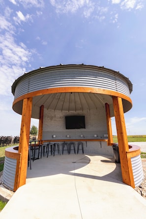 Une structure circulaire en plein air, dotée d’un toit plat, de piliers en bois et d’un mur en métal.