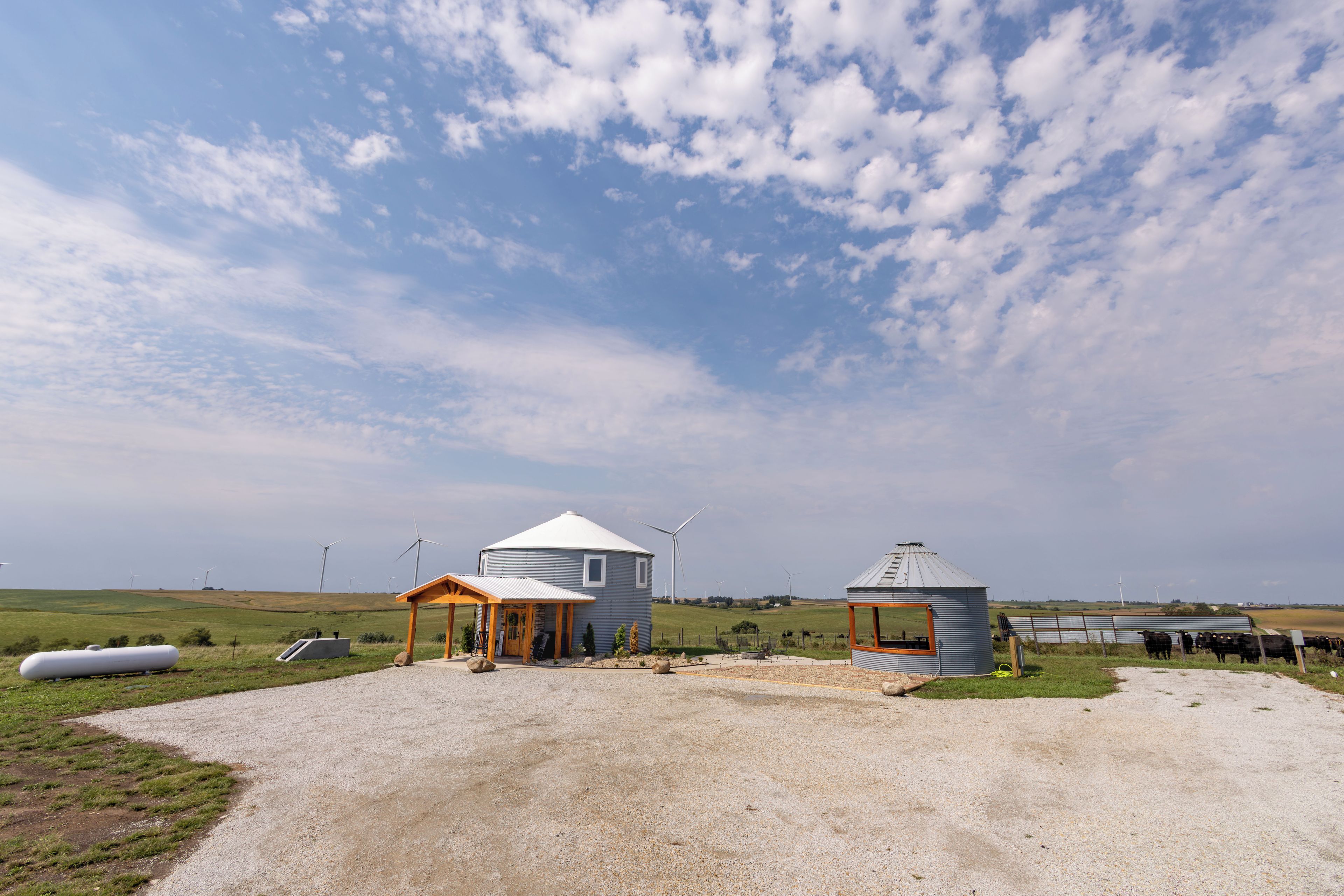 Paisaje rural con dos yurtas, una pequeña construcción de madera y un rebaño de ganado.