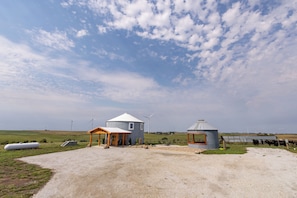 A rural landscape with two yurts, a small wooden structure, and a herd of cattle.