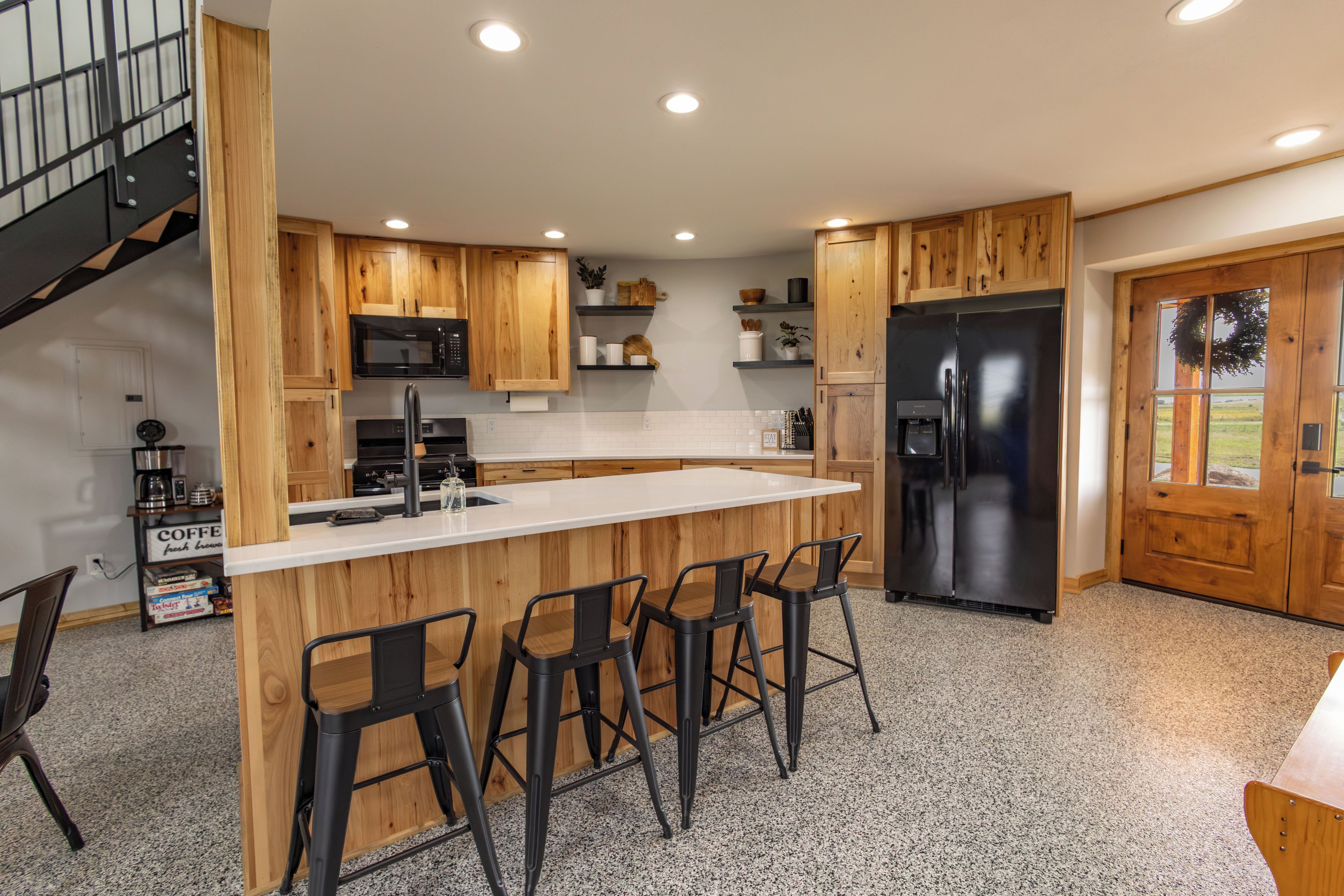 A kitchen with wooden cabinets, a stainless steel refrigerator, a bar area with stools, and a staircase.