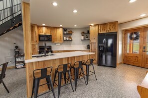A kitchen with wooden cabinets, a stainless steel refrigerator, a bar area with stools, and a staircase.