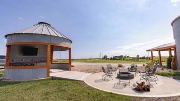 Ein Pavillon mit Grill und Sitzbereich im Freien, umgeben von einer Wiese und Windkraftanlagen im Hintergrund.