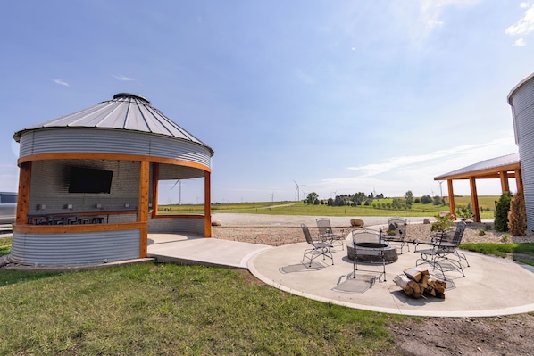 Un belvédère doté d’un barbecue et d’un espace salon extérieur, entouré d’un champ verdoyant et avec des éoliennes en arrière-plan.