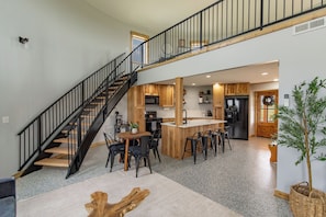 Une cuisine moderne avec un îlot central, des appareils électroménagers noirs et un escalier en bois.
