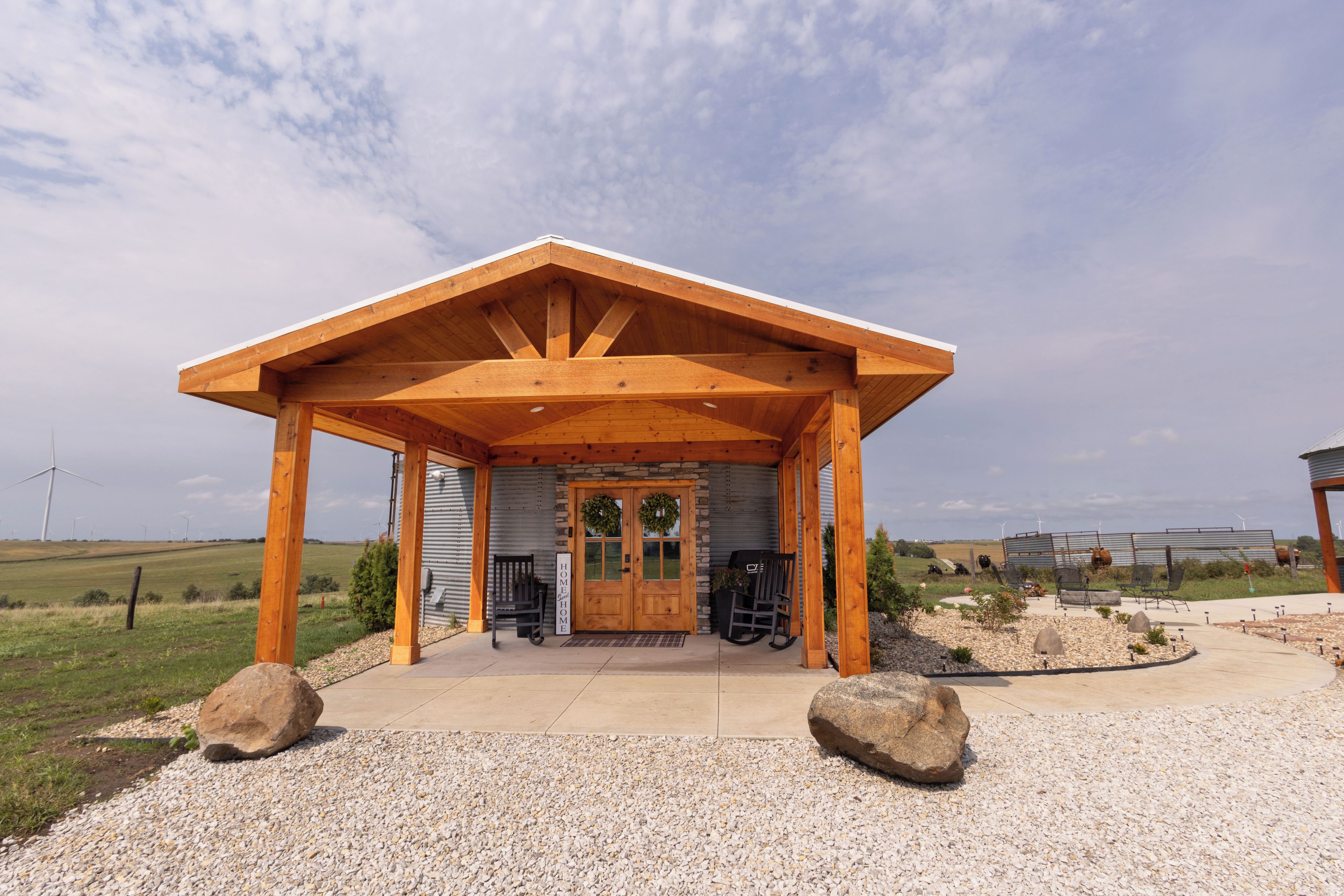 Un pavillon en bois avec une entrée en pierre, un banc et une pancarte sur laquelle on peut lire : « Chez soi, quel bonheur ! »