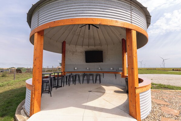 A covered outdoor seating area with a central table and multiple stools.