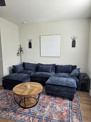 Ein modernes Wohnzimmer mit einem Ecksofa, einem runden Holztisch, einem gemusterten Teppich und Wanddekoration.