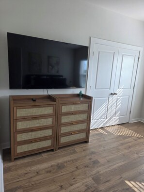 Een kamer met een grote flatscreen televisie aan de muur, een houten kast met lades en een witte deur met raam.
