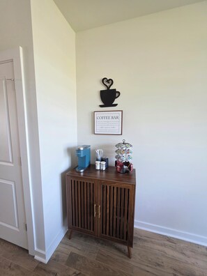 A coffee bar setup with a coffee maker, cups, and a coffee-themed sign on a wooden cabinet. - Bright & Cozy 3BR Near Historic Summerville (Summerville)