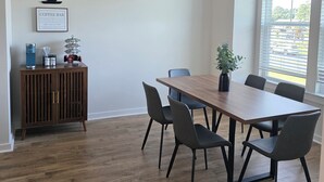 A conference room with a wooden table, six chairs, a cabinet with a coffee-themed decoration, and a window with blinds. - Bright & Cozy 3BR Near Historic Summerville (Summerville)