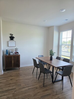 Ein Konferenzraum mit Holztisch, sechs Stühlen, einem Schrank mit Kaffeemotiv und einem Fenster mit Jalousien.