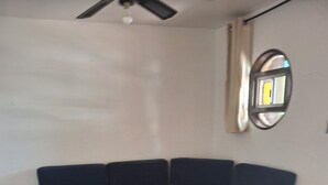 A room with a sectional sofa, a ceiling fan, and a round mirror on the wall.