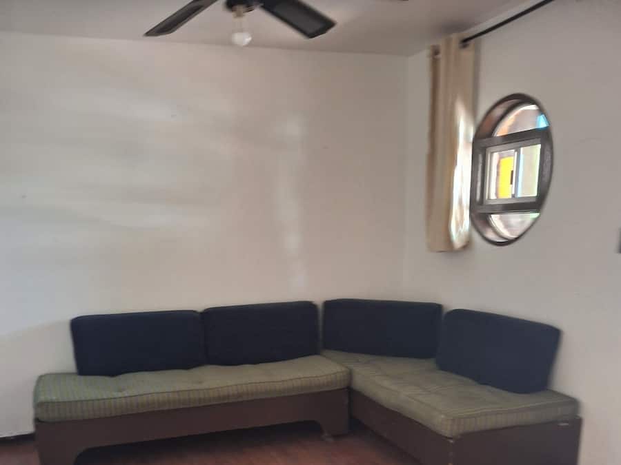 A room with a sectional sofa, a ceiling fan, and a round mirror on the wall.