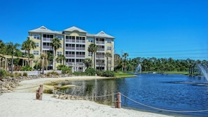 Ein mehrstöckiges Hotel mit Balkonen, einem Sandstrand und einem Wasserbecken mit einer Springbrunnen.