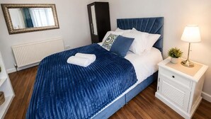 A bedroom with a bed, a nightstand, a lamp, a mirror, and a radiator. - Mauldeth Boutique House (Manchester)