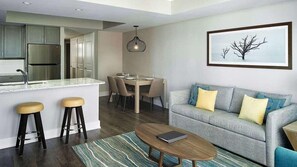 Una sala de estar moderna con un sofá gris, dos taburetes de madera, una mesa de centro y un comedor con una mesa y sillas.