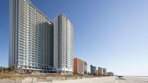 A beachfront hotel with multiple high-rise buildings, a sandy beach, and a clear sky.