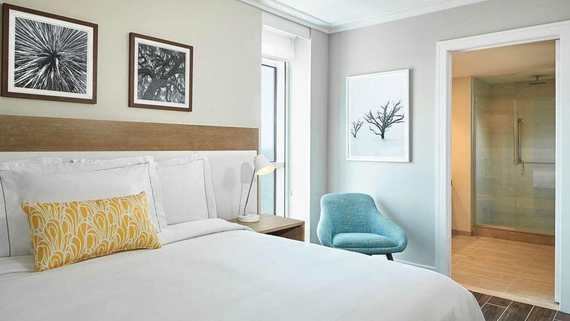 Habitación de hotel con una cama grande, una mesita de noche, una lámpara de escritorio, una silla y zona de ducha.