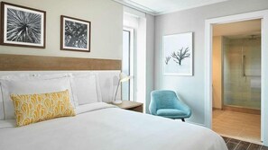 Ein Hotelzimmer mit einem großen Bett, einem Nachttisch, einer Schreibtischlampe, einem Sessel und einer Dusche.