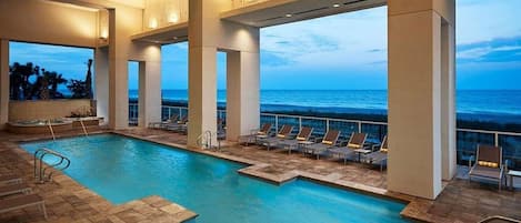 An indoor swimming pool with clear views of the ocean, lounge chairs, and a sun terrace.