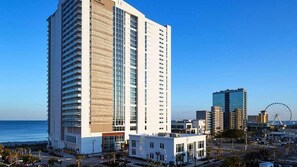Ein hoch aufragendes Hotel mit modernem Design, nahe eines Uferbereichs, im Hintergrund ein Riesenrad.