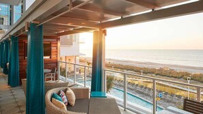 A balcony with wicker furniture, a pool, and a view of the beach.