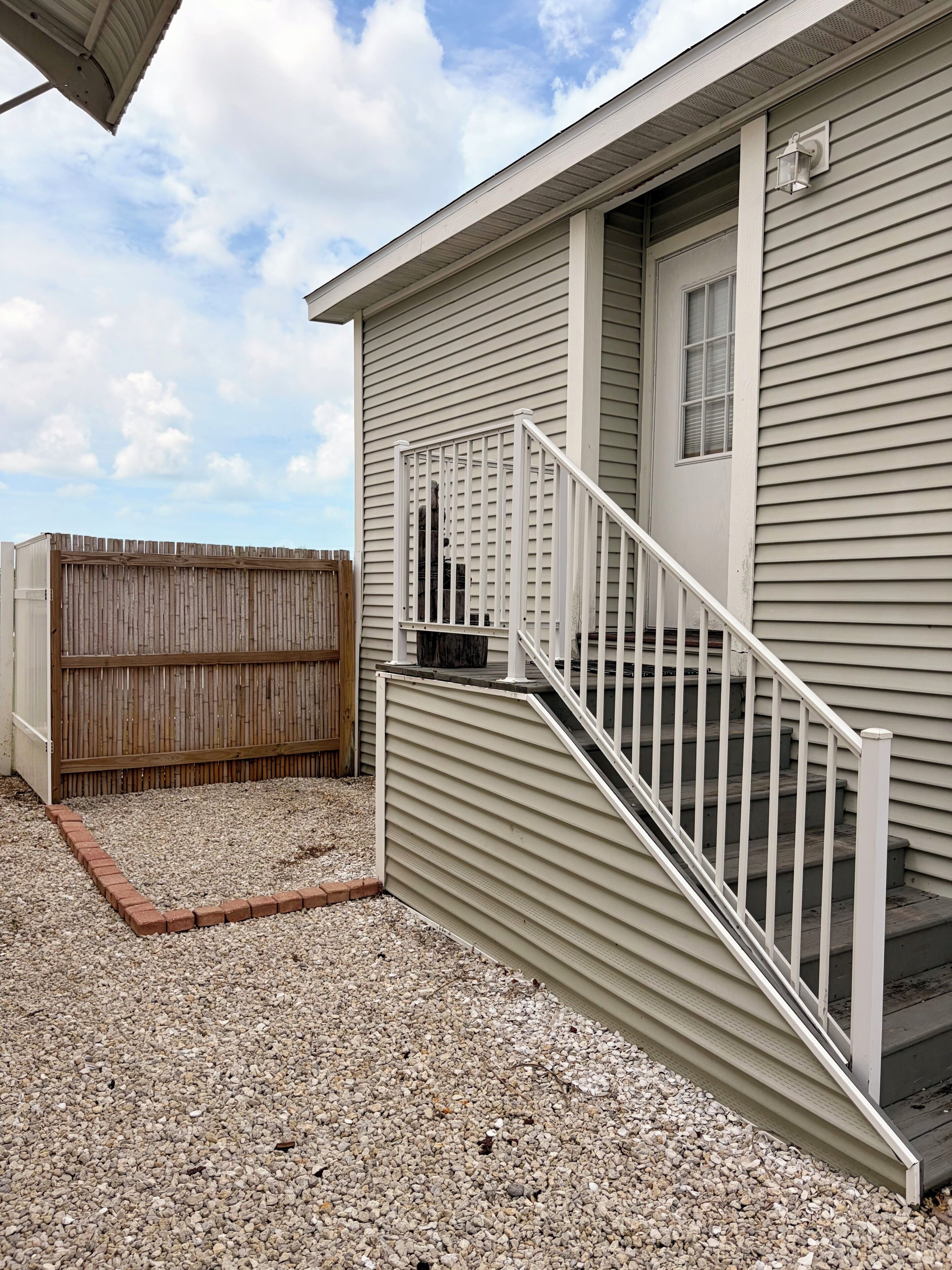 A residential building with a wooden fence, a gravel driveway, and a white staircase leading to a door.
