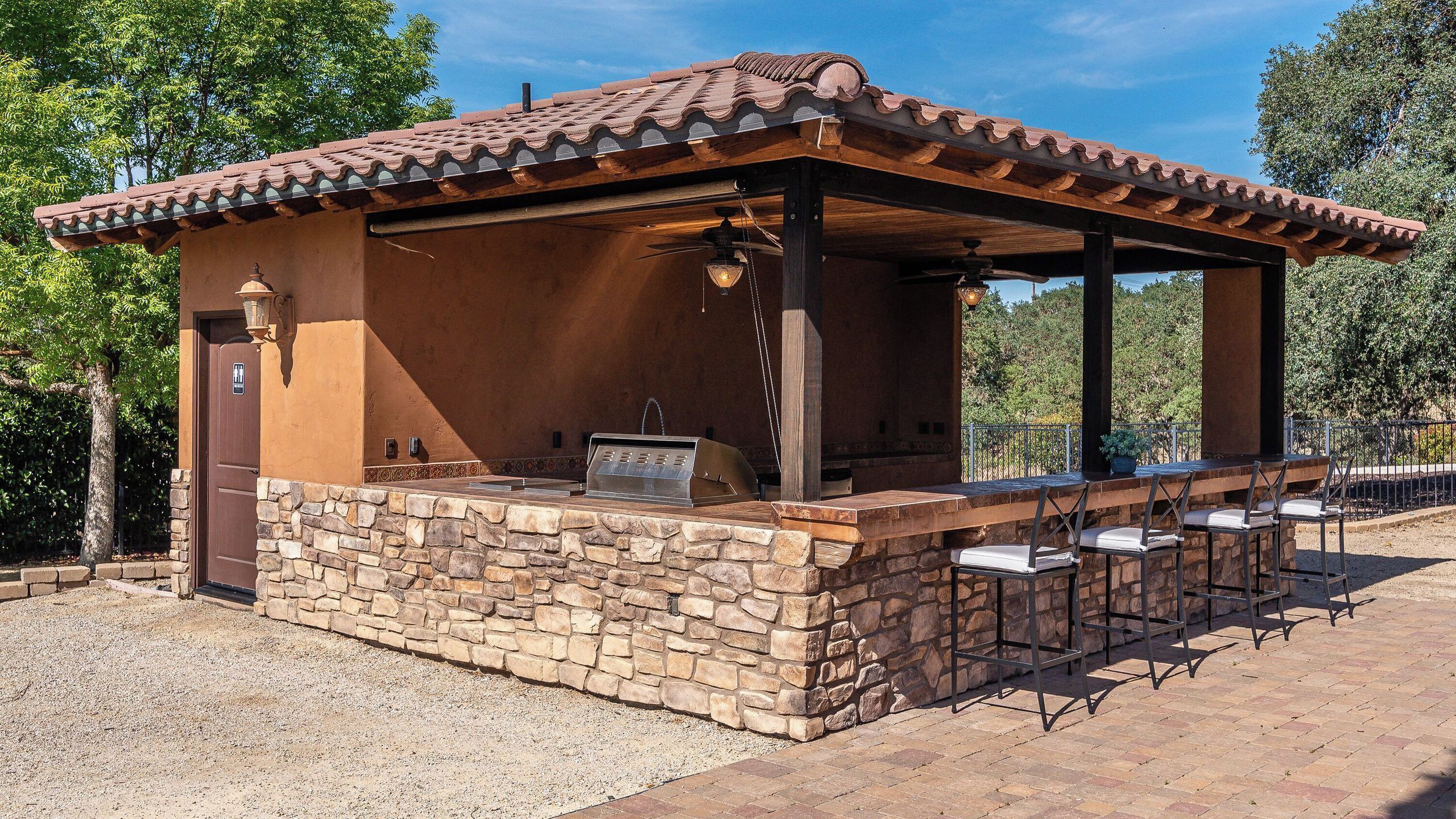 An outdoor barbecue area with stone walls, a tiled roof, and a pergola.
