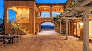 Un'ampia terrazza esterna con pavimento in mattoni, una scala che conduce a un livello superiore e vista sul paesaggio sullo sfondo.