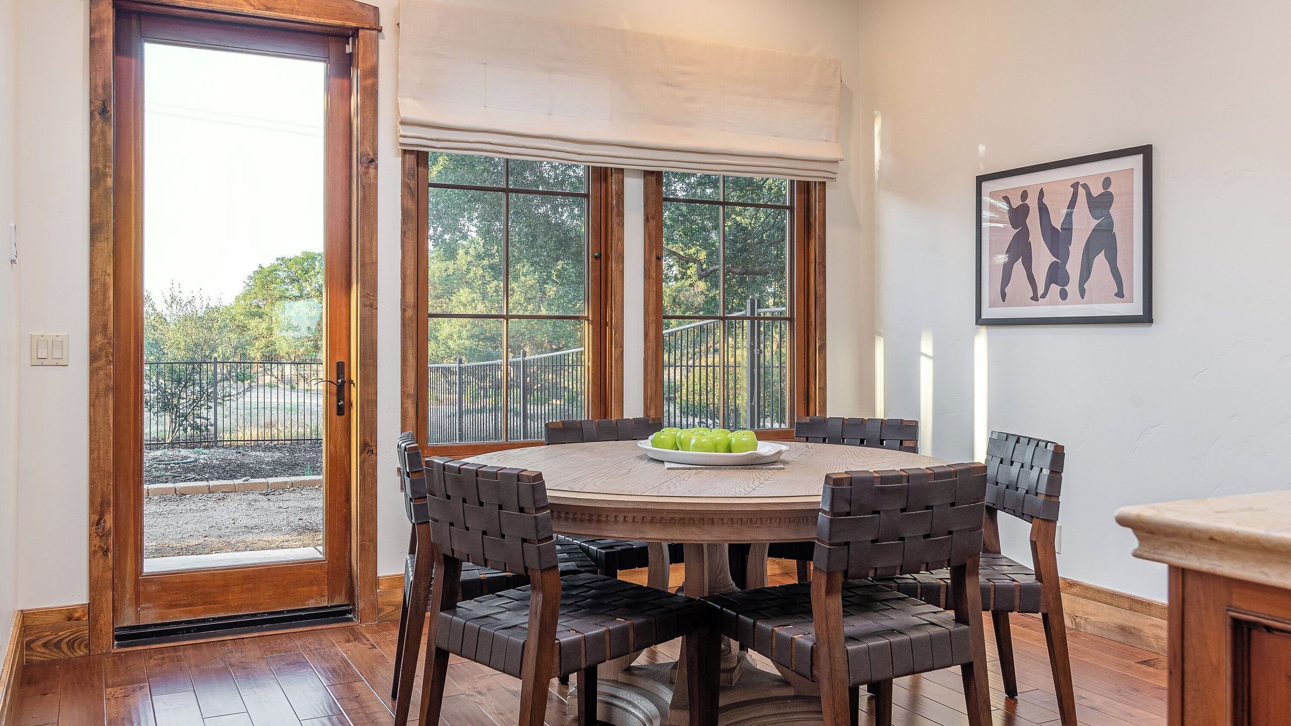 A dining area with a round wooden table, four chairs, and a plate of green apples.