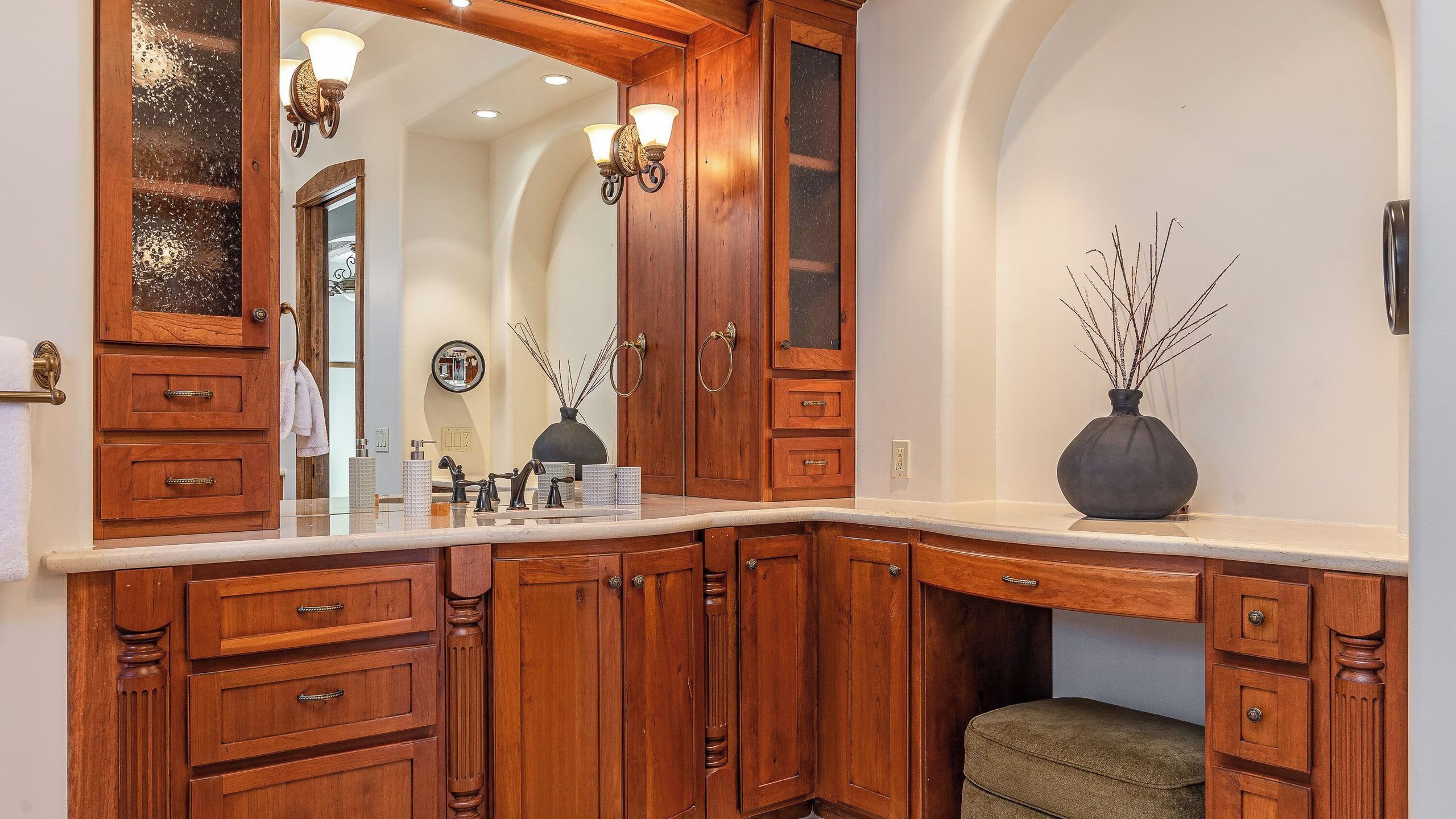 Un baño con muebles de madera, un espejo grande, un lavamanos y dos apliques de pared.