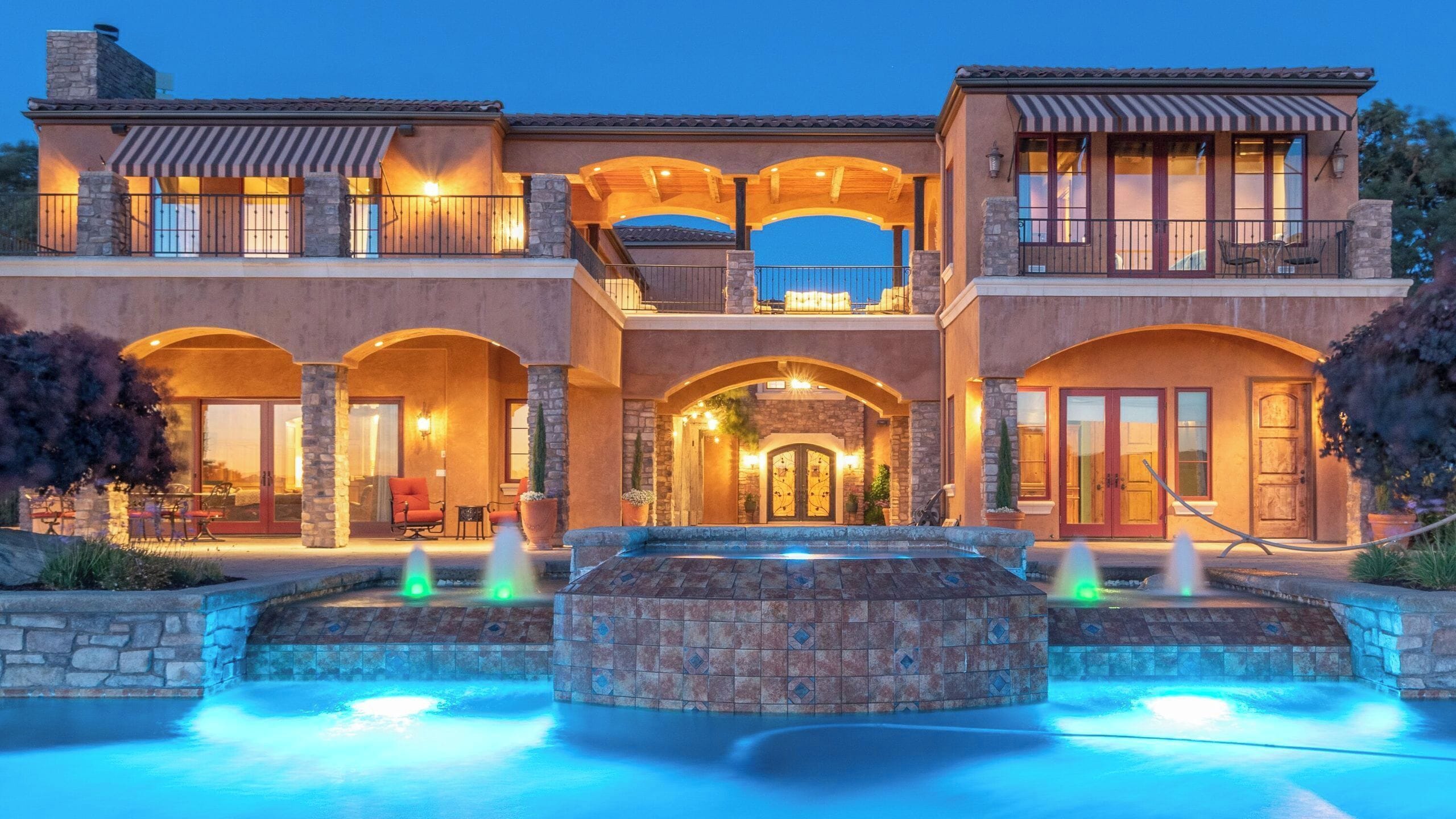 A multi-story house with a swimming pool and a fountain.