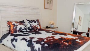 A bed with a patterned bedspread, a bedside table with a vase of flowers, and a mirror on the wall.