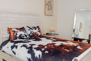 A bed with a patterned bedspread, a bedside table with a vase of flowers, and a mirror on the wall.