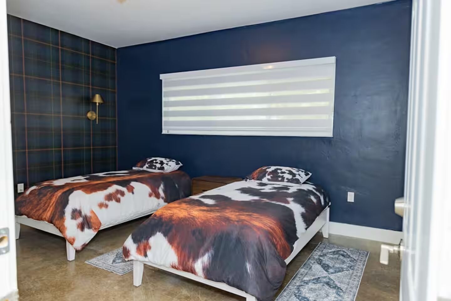 Un dormitorio con dos camas, una ventana con persianas, un papel tapiz estampado y una alfombra.