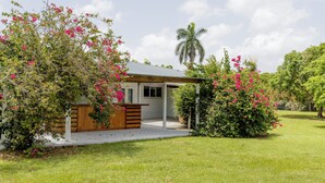 A small house with a covered porch, surrounded by lush greenery and flowering plants.