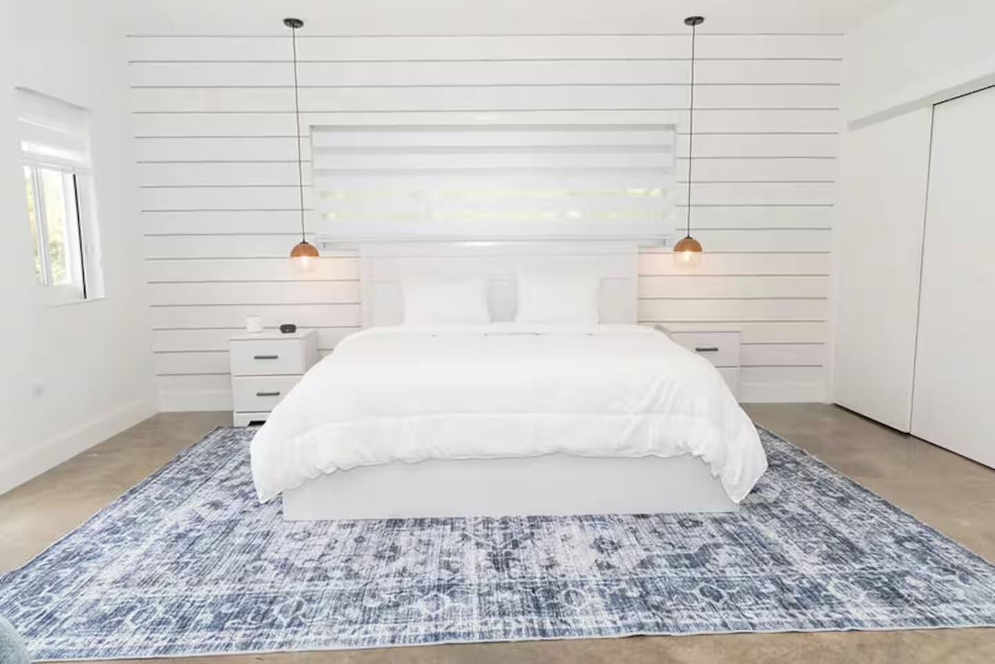 A bedroom with a bed, two bedside tables, and a patterned rug.