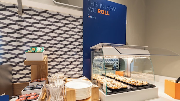 A buffet area with a display of cinnamon sweet rolls, a sign indicating the roll selection, and a patterned wall in the background.