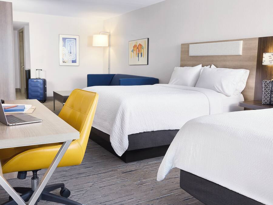 A hotel room with two beds, a desk with a laptop, a chair, and a suitcase.