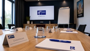 A conference room with a wooden table, nameplates, a projector screen displaying the hotel logo, and a whiteboard. - Holiday Inn Express Troyes Gare By Ihg (Troyes)