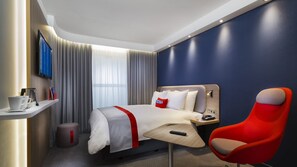A hotel room with a bed, a red chair, a bedside table with a phone, a TV on the wall, and a window with curtains. - Holiday Inn Express Troyes Gare By Ihg (Troyes)