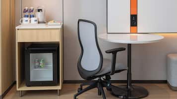 A compact workspace with a modern chair, a small refrigerator, and a table with a lamp.
