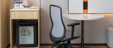 A compact workspace with a modern chair, a small refrigerator, and a table with a lamp.