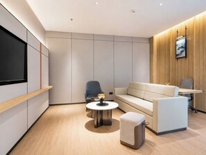 A modern room with a sofa, armchair, round table, and a TV mounted on the wall. - Holiday Inn Express Dujiangyan Ctc By Ihg (Chengdu)