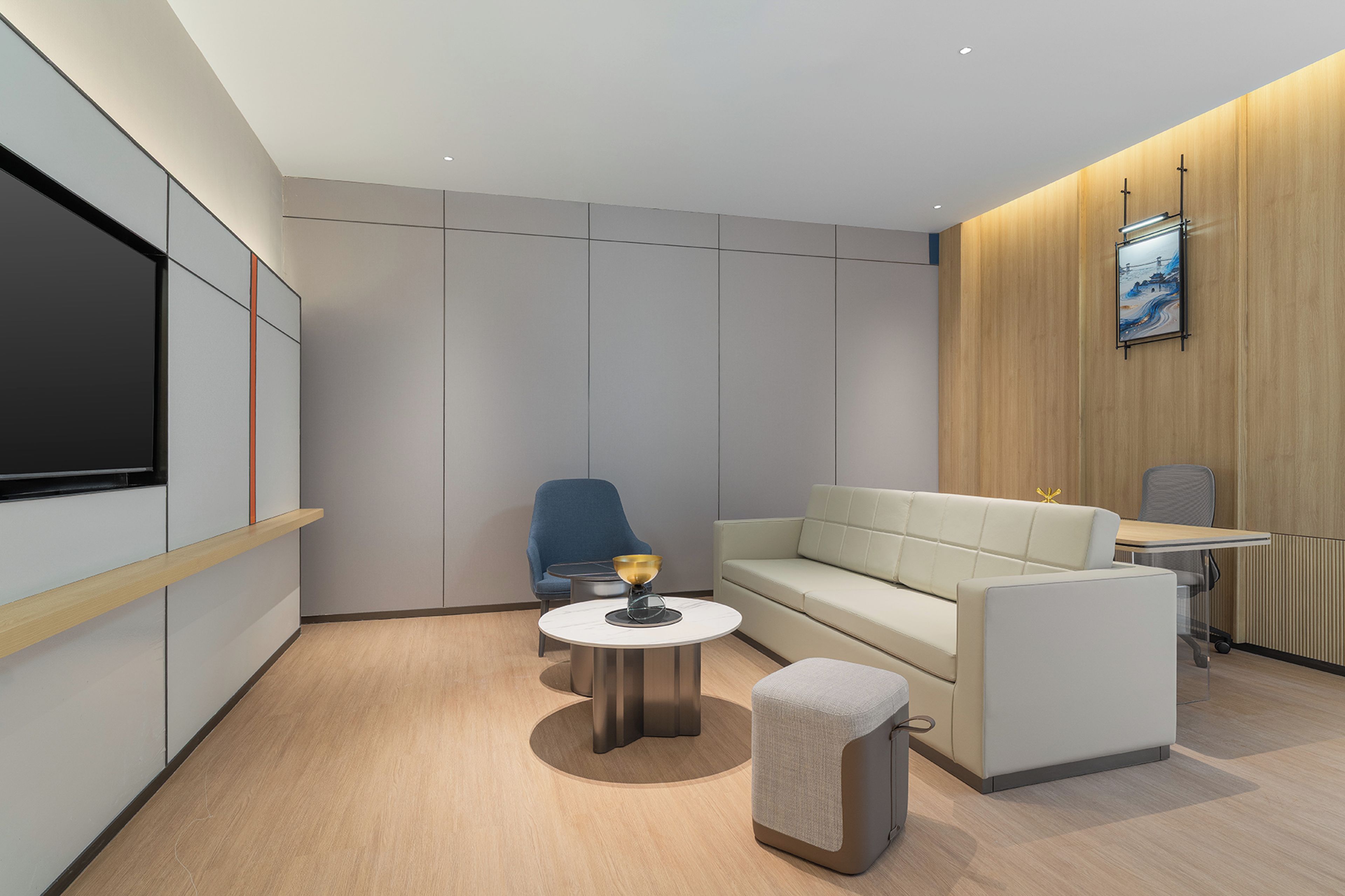 Uma sala de estar moderna com um sofá, uma mesa redonda pequena, uma cadeira azul e uma televisão fixada na parede.