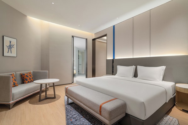 Una habitación de hotel moderna con una cama grande, un sofá, una mesita y un banco.