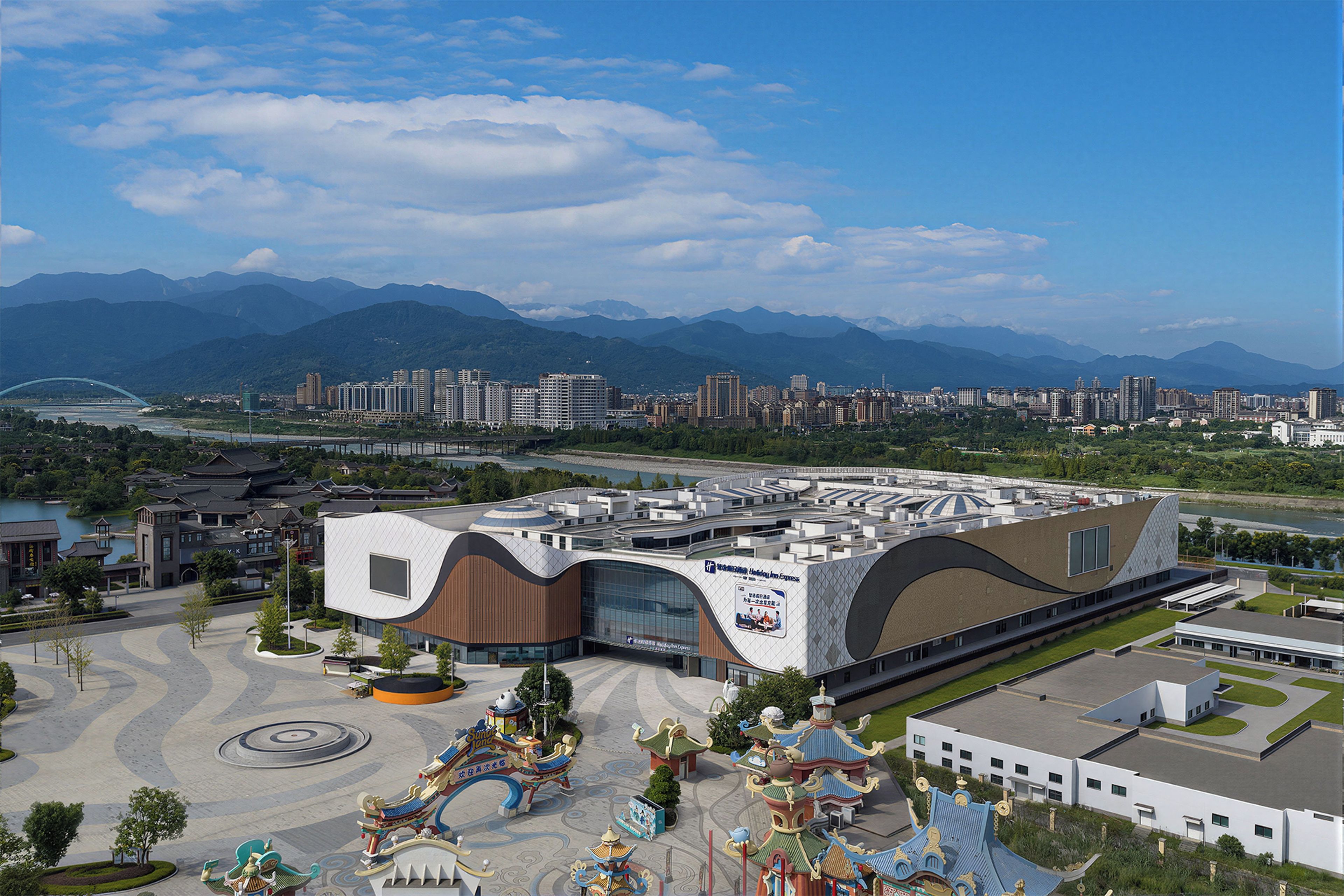 A modern building with a curved facade, surrounded by a landscaped area with a decorative fountain and traditional-style structures.